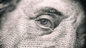 A close up of Benjamin Franklin's eye peering out from a 100 dollar bill.