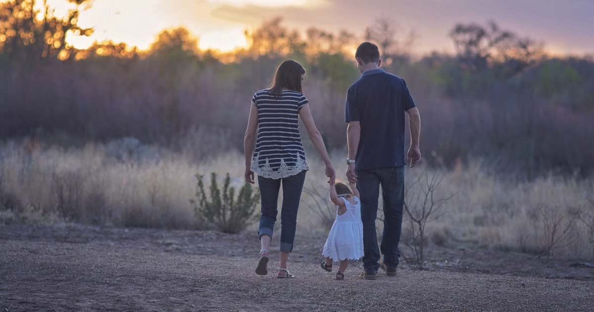 Mother & Father Walking Hand-in-Hand with Toddler Girl at Sunset