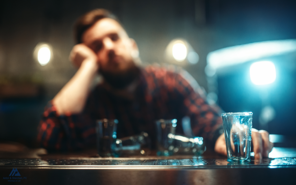 A man slumped over at a bar surrounded by empty shot glasses.