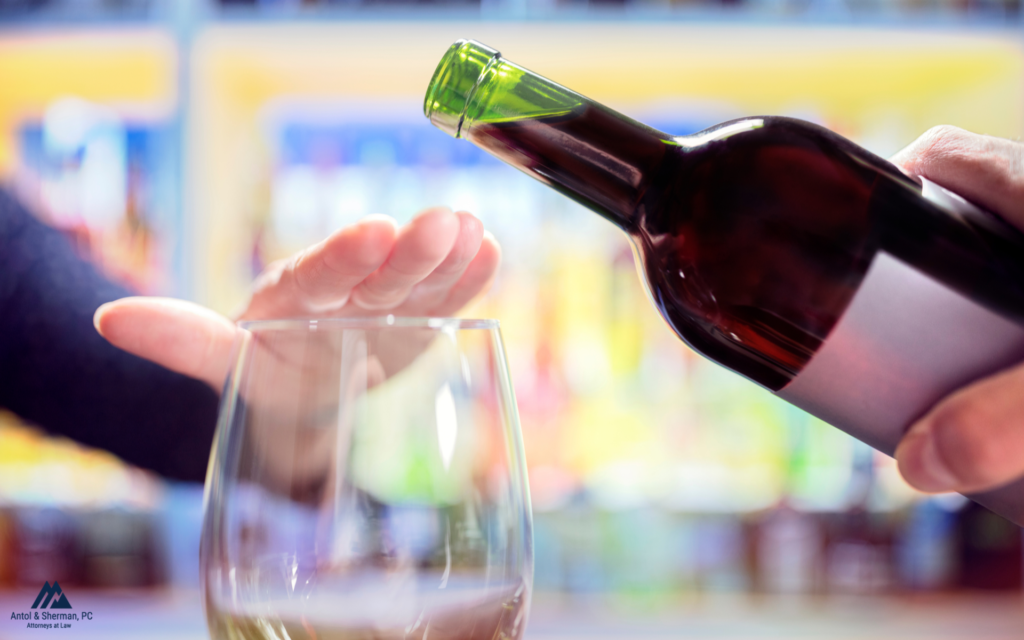 An image of a glass and wine bottle with someone putting their hand over the wine glass so wine cannot be poured.