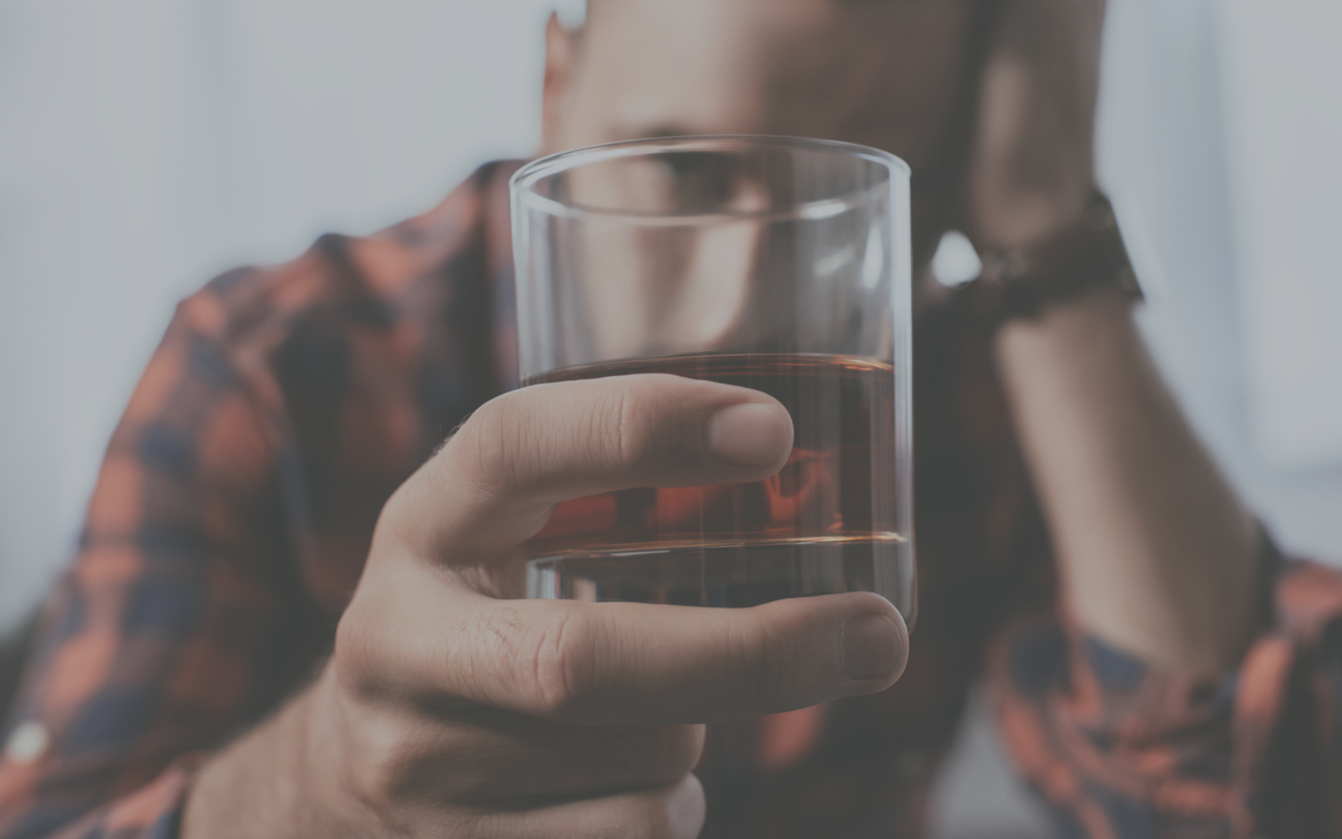 A man looking through a glass of dark liquor.