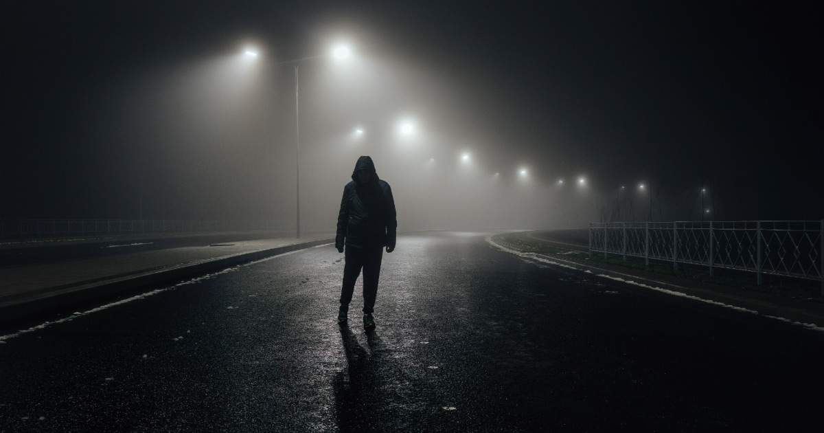 Silhouette of a man standing ominously in a park at night