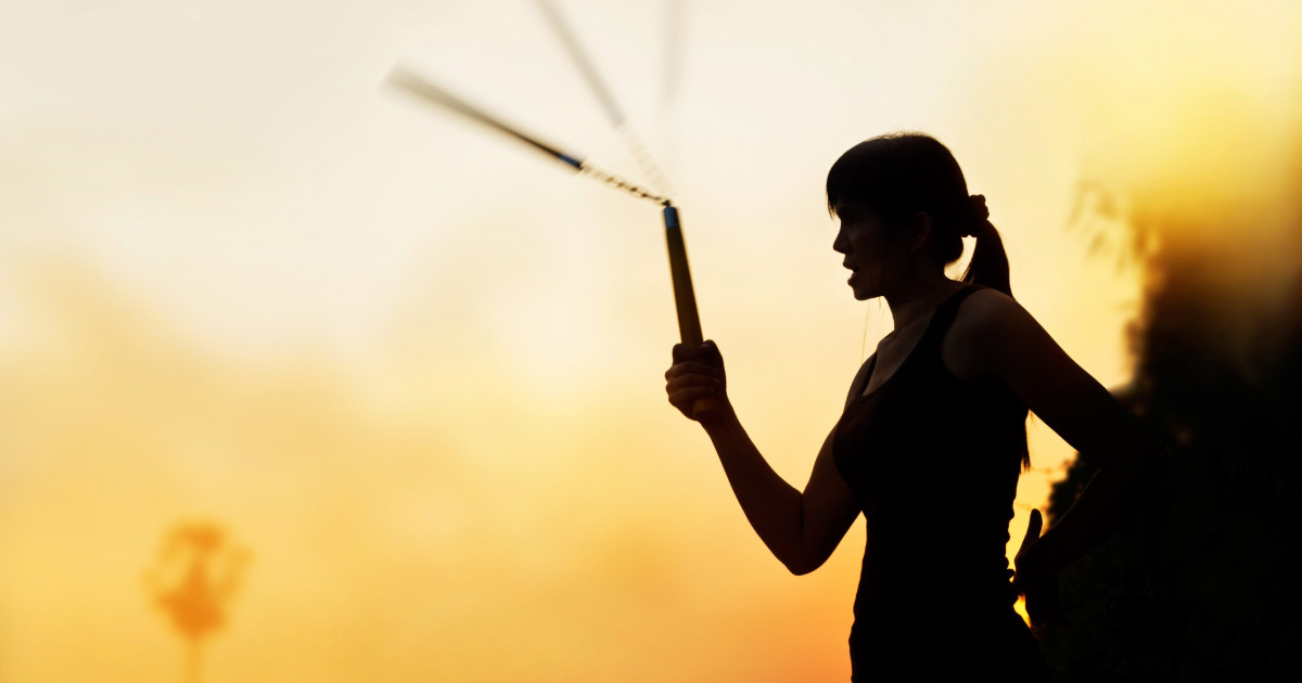 Silhouette of woman practicing nunchuck skills