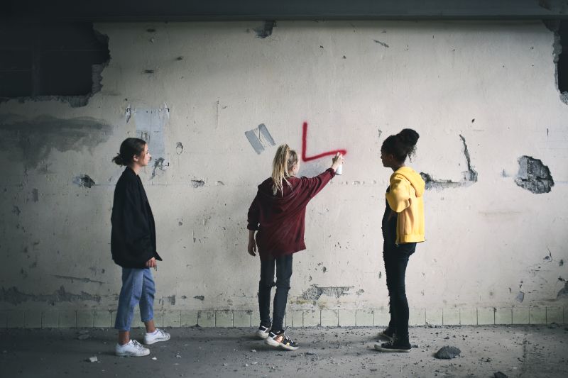 Three teenage girls vandalizing a wall with spray paint.