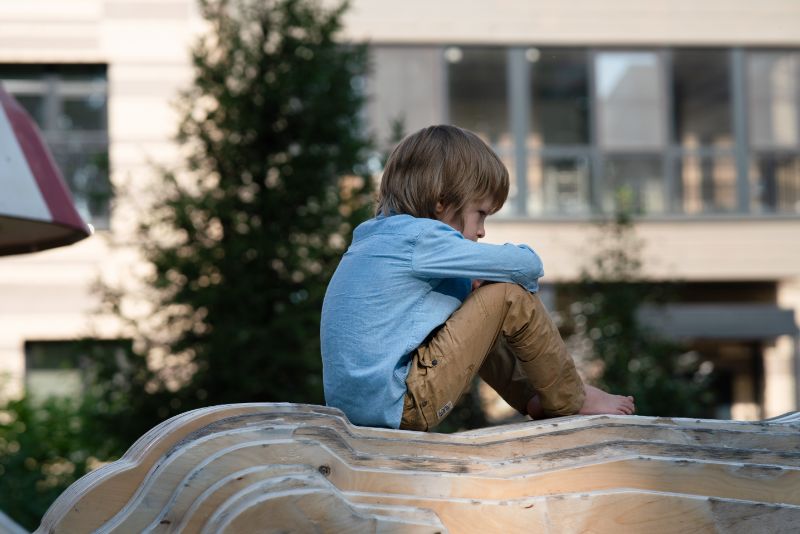 Child of divorce sits sadly on the playground.