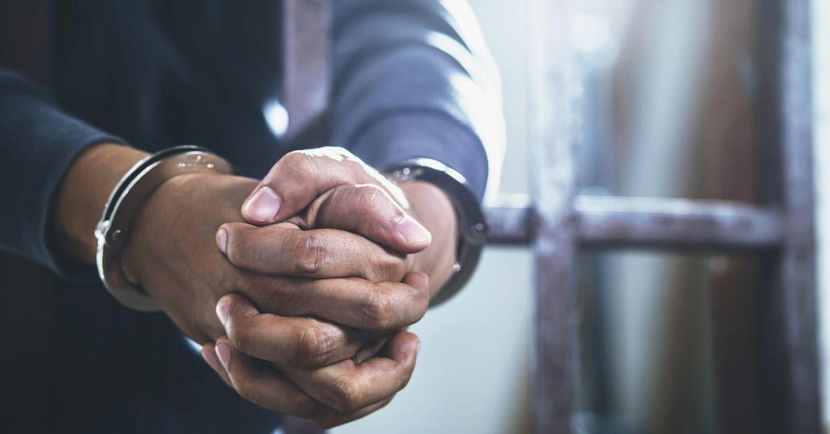 Man Holding Handcuffed Hands Through Jail Bars