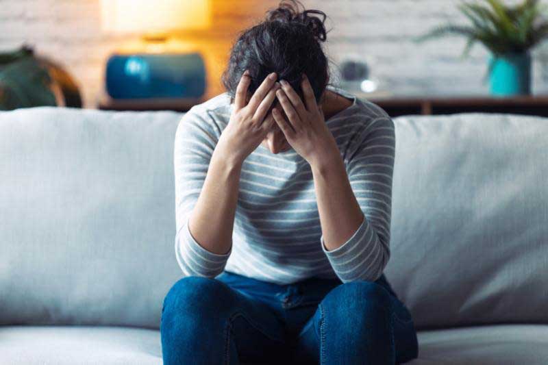 Woman Holding Hands on Head Sitting on Couch