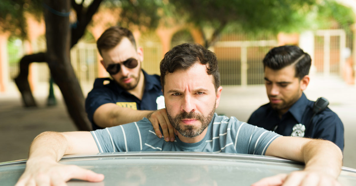 Man with hands on roof of car being arrested by two officers