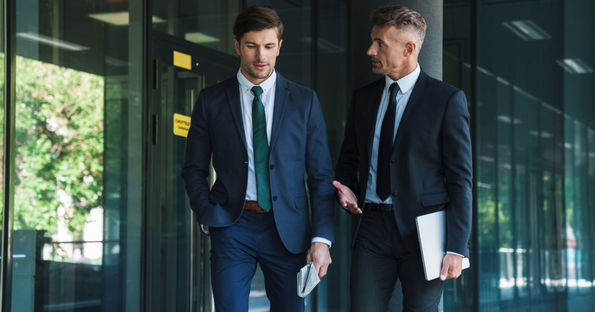 Two men in suits holding paperwork having a discussion